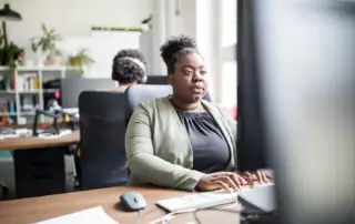 A woman working at her desk, with another person working behind her